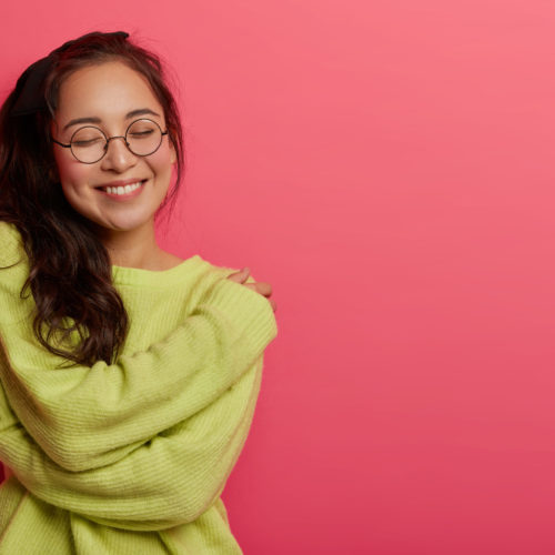 Photo Of Charming Woman Expresses Self Love And Care, Enjoys Wearing New Soft Green Sweater, Embraces Own Body, Recalls Romantic Moment With Boyfriend, Smiles Pleasantly, Stands Over Rosy Wall Photo Of Charming Woman Expresses Self Love And Care, Enjoys Wearing New Soft Green Sweater, Embraces Own Body, Recalls Romantic Moment With Boyfriend, Smiles Pleasantly, Stands Over Rosy Wall