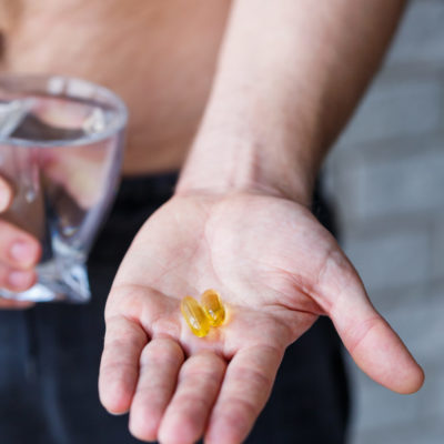 A Young Man Holds Vitamins And A Glass Of Water In His Hands. Immunity Pills A Young Man Holds Vitamins And A Glass Of Water In His Hands. Immunity Pills