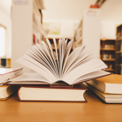 Book In Library With Old Open Textbook, Stack Piles Of Literatur Book In Library With Old Open Textbook, Stack Piles Of Literatur
