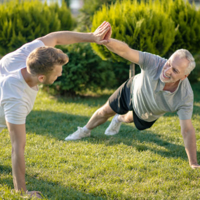 Brown Haired Male And Grey Haired Male Standing In Plank Pose, Giving High Five Brown Haired Male And Grey Haired Male Standing In Plank Pose, Giving High Five