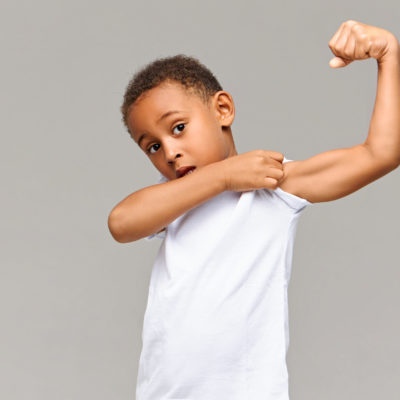 Look At My Bicep. Picture Of Funny Afro American In Casual White T Shirt Posing Isolated At Gray Studio Wall Pulling Up Sleeve, Showing His Tensed Arm Muscle. Childhood, Fitness And Sports Concept Look At My Bicep. Picture Of Funny Afro American In Casual White T Shirt Posing Isolated At Gray Studio Wall Pulling Up Sleeve, Showing His Tensed Arm Muscle. Childhood, Fitness And Sports Concept