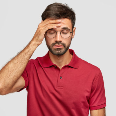 Overworked Cuacasian Male Feels Terrible Headache After Sleepless Night, Keeps Hand On Forehead, Shut Eyes, Dressed In Casual Red T Shirt, Stands Against White Background. People And Tiredness Overworked Cuacasian Male Feels Terrible Headache After Sleepless Night, Keeps Hand On Forehead, Shut Eyes, Dressed In Casual Red T Shirt, Stands Against White Background. People And Tiredness