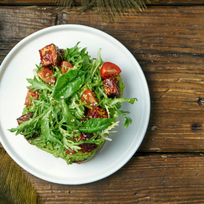 Trend Street Food Avocado Toast With Guacamole, Arugula And Tofu Cheese In A White Plate On A Wooden Background. Vegetarian Food Trend Street Food Avocado Toast With Guacamole, Arugula And Tofu Cheese In A White Plate On A Wooden Background. Vegetarian Food